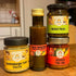 Vier große Gläser (Klassik-Senf, Möhren-Piri-Piri, Kräuterpesto, Teufelszeug) als veganes Probier-Set, arrangiert in natürlicher Küchen- oder Holzoptik – mild bis scharf.